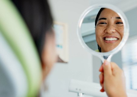 Woman smiling at reflection in dentist office