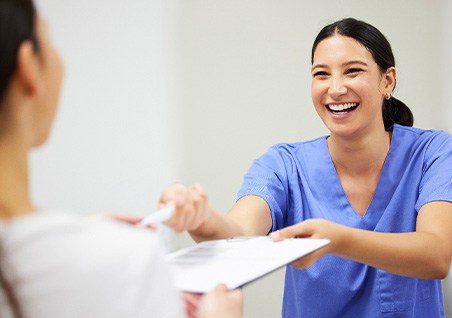 Dental assistant smiling while giving patient a clipboard