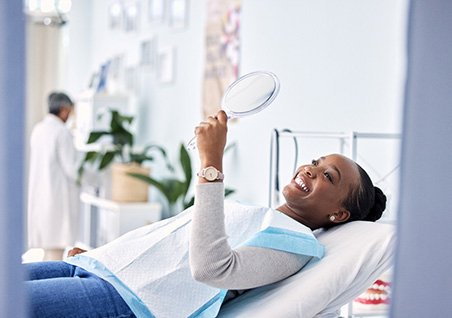 Woman smiling at reflection in handheld mirror