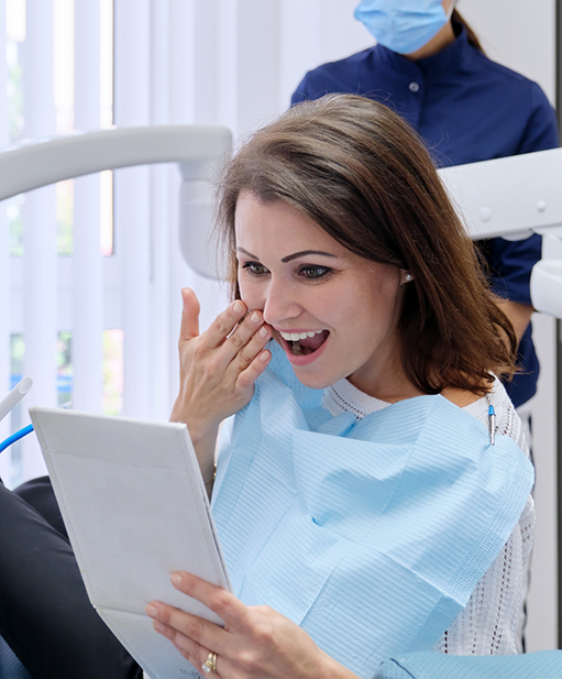 Woman admiring her new smile in a mirror after cosmetic dentistry in Bellaire