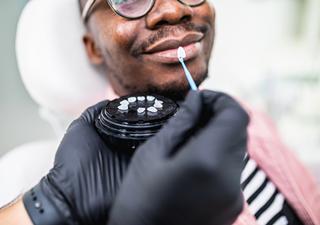 Dentist holding a veneer in front of a smiling patient