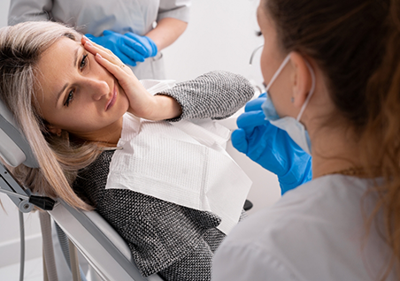 Woman holding her cheek in pain while talking to her emergency dentist