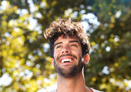 Young man with curly dark hair smiling outdoors