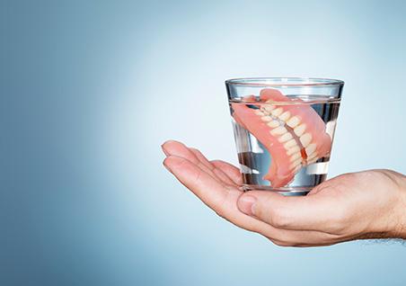 Dentures in a glass of water on a hand