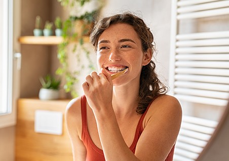 Woman in burnt orange tank top brushing her teeth