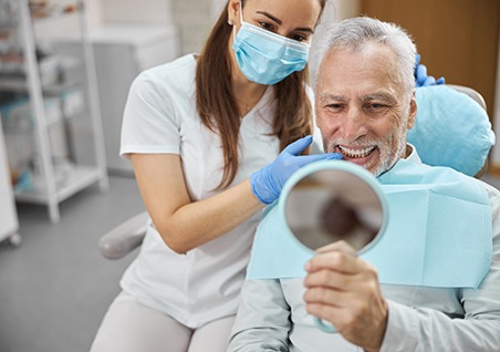 Man with white hair in dental chair with dentist looking at teeth in mirror