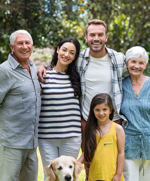 Three generations of a smiling family with green trees in the background