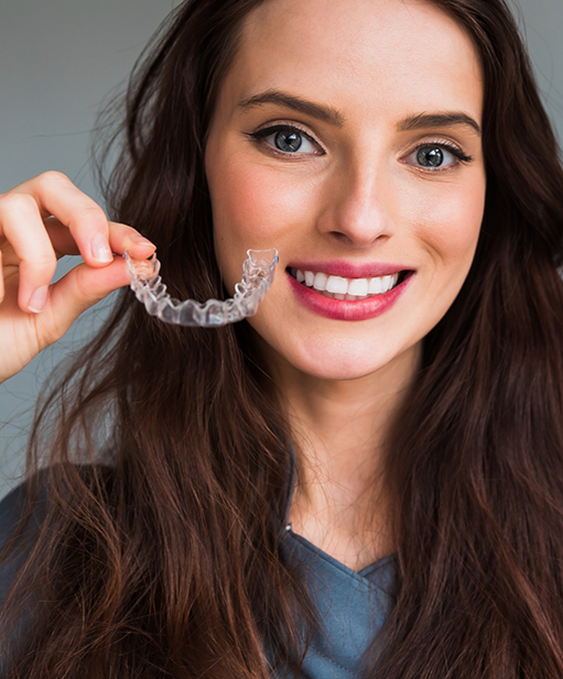 Smiling woman holding an Invisalign clear aligner in Bellaire