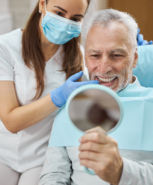 Senior man admiring his smile in a mirror after replacing missing teeth in Bellaire