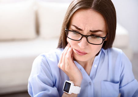 Woman wincing in pain and holding the side of her jaw